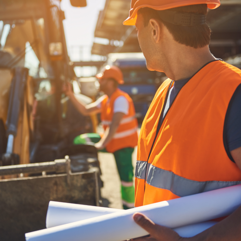 Two men in construction hats and vests  standing at a construction site beside a truck