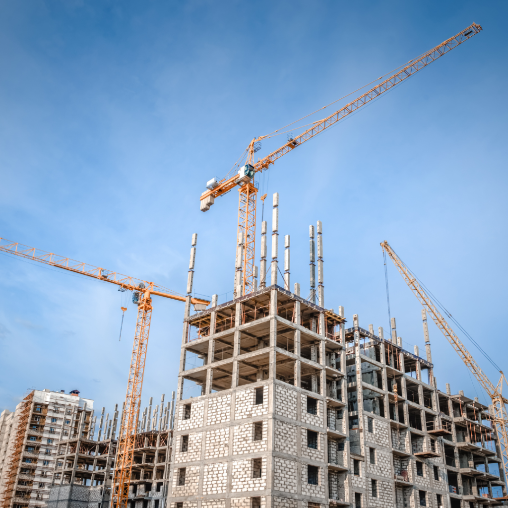 A high building topped with cranes and the blue sky as a backdrop