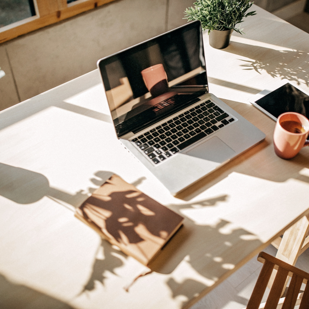 A shiny laptop on a nice desk with a little potted plant; in the shine of the laptop screen, a lone teacup is reflected