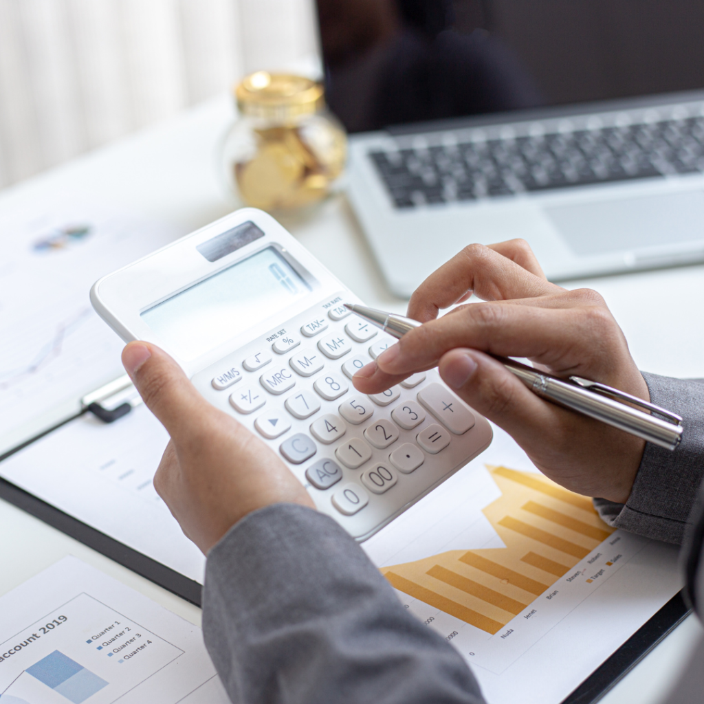 someone holding a pen, poised to type numbers into a white calculator 